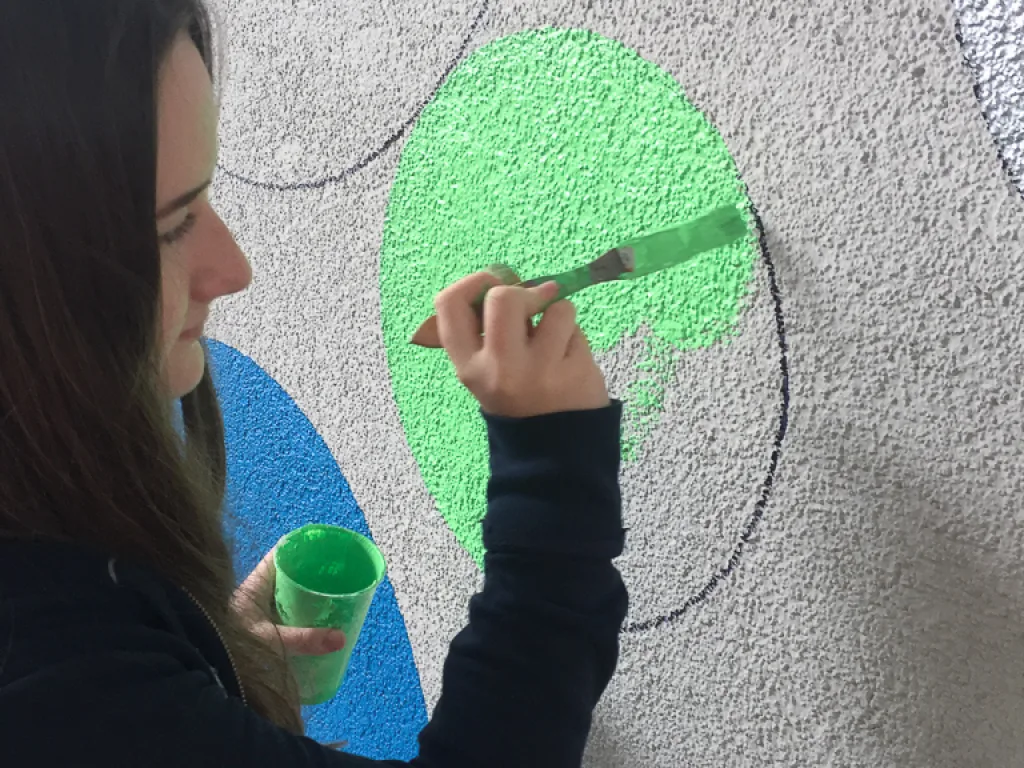 Person malt einen grünen Kreis an eine Wand.